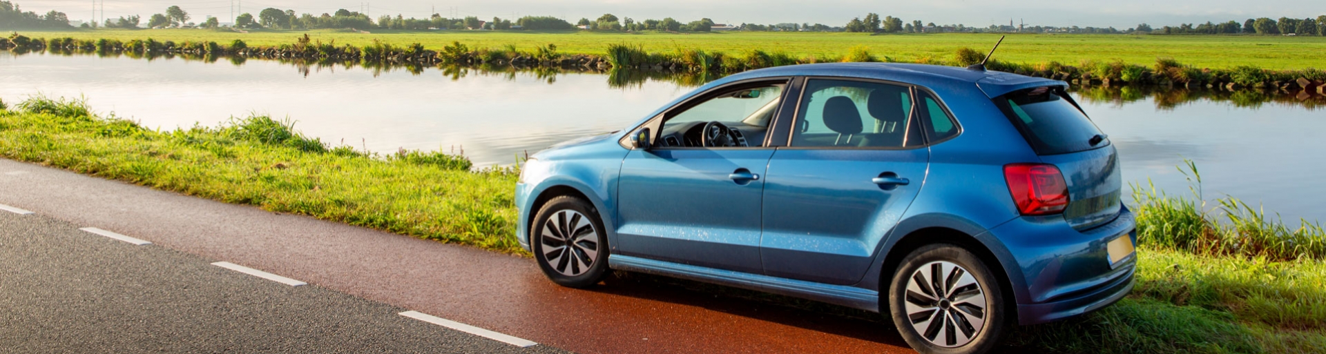 Een blauwe auto staat geparkeerd langs de kant van de weg op een bewolkte dag in Nederland.